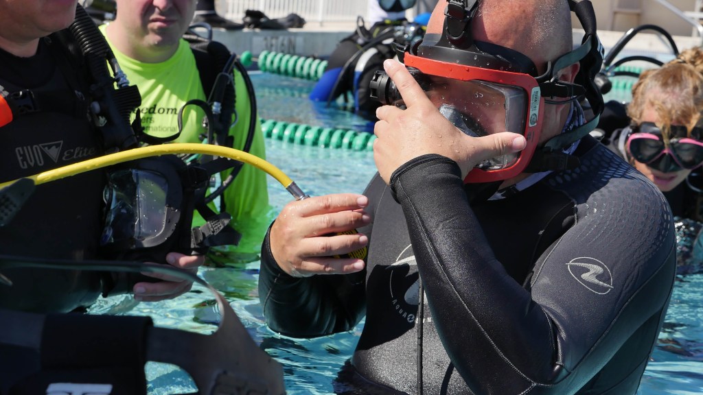 - N9BO℠ | Global Underwater Services Ltd Several people in wetsuits and scuba masks stand in a swimming pool, one person adjusting their full-face mask while another holds a yellow air hose. Pool lane dividers are visible in the background.