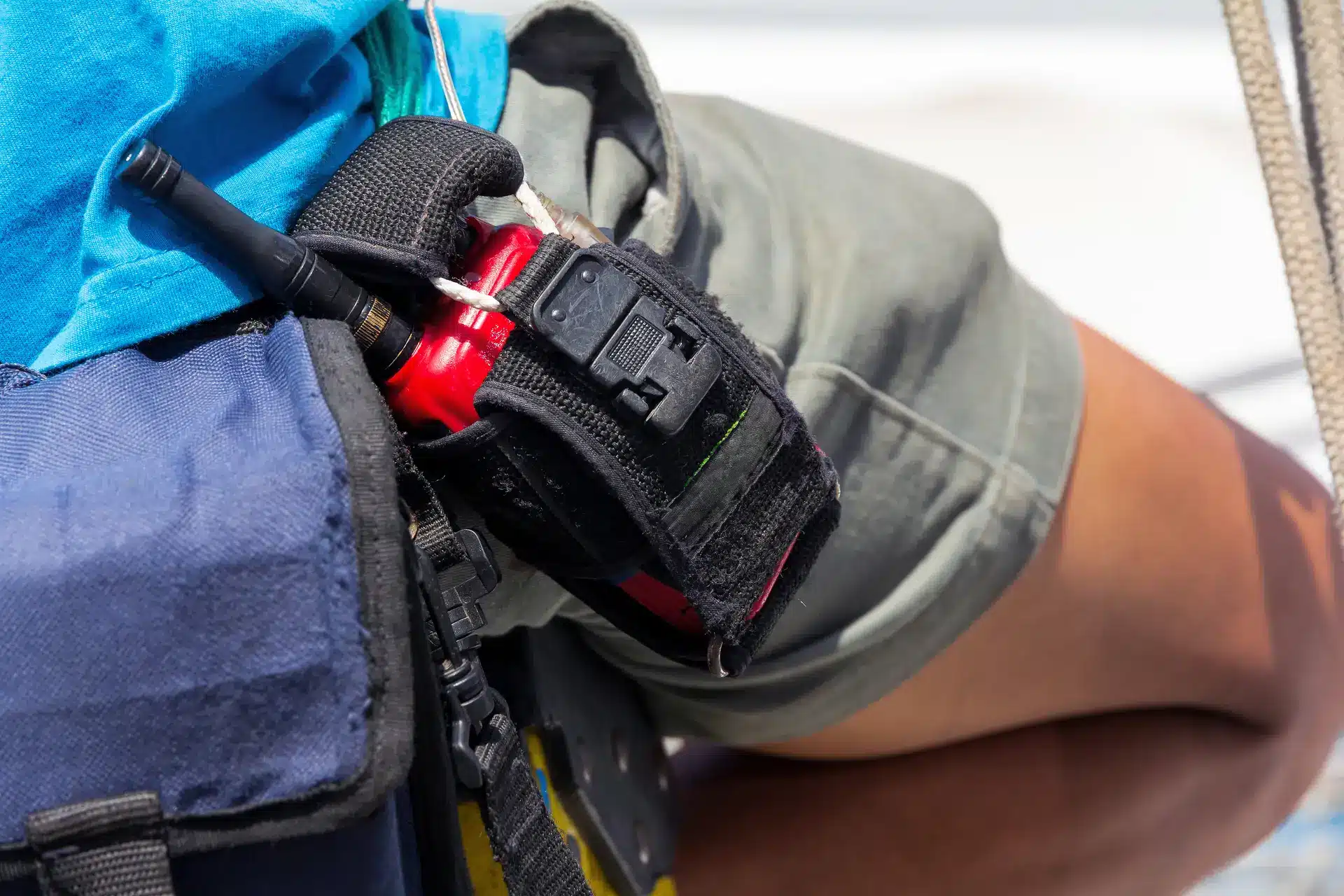Close-up of a person wearing a blue shirt and grey shorts with a black holder attached to their belt, carrying a red handheld radio or walkie-talkie.