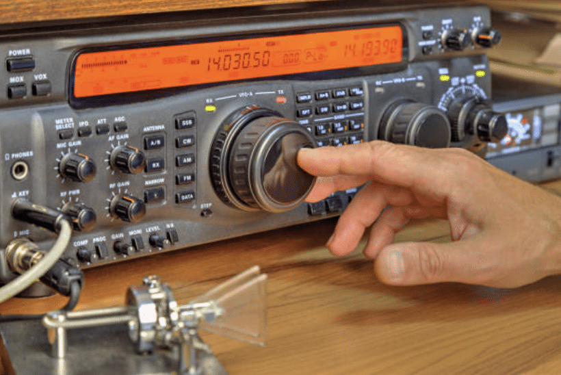 Screenshot 2026-03-14 at 115032 - N9BO℠ | Global Underwater Services Ltd A hand adjusts the main knob on a ham radio transceiver, with various buttons, dials, and a digital display showing frequency numbers. A Morse code key is visible in the foreground.