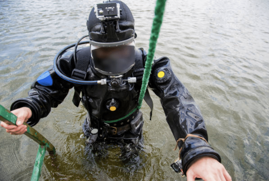 Screenshot 2026-03-14 at 135654 - N9BO℠ | Global Underwater Services Ltd A person in a black diving suit and helmet with a camera climbs out of the water using a green rope, with one hand holding a metal ladder. The face is blurred.
