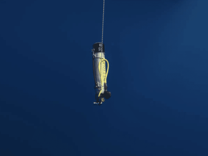 A scuba diver in full kit hangs vertically underwater, attached to a safety line, surrounded by deep blue sea.