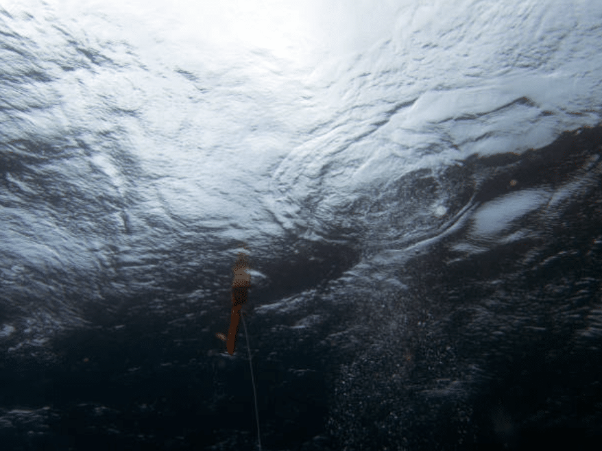 Screenshot 2026-03-15 at 170154 - N9BO℠ | Global Underwater Services Ltd Underwater view looking up at the water’s surface, showing a fishing lure or float suspended on a line, with light coming through the rippling water above.