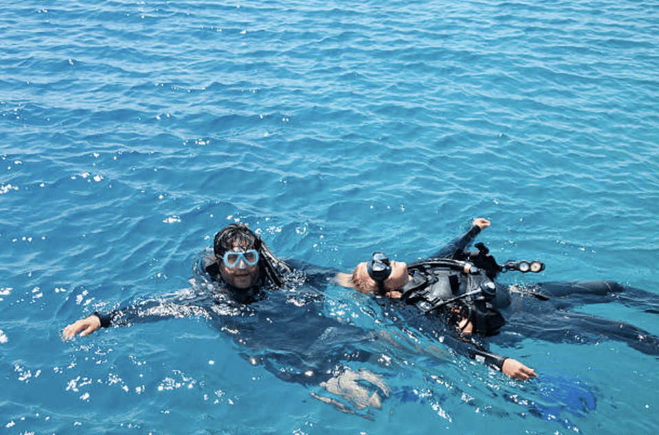 Screenshot 2026-03-15 at 214742 - N9BO℠ | Global Underwater Services Ltd Two scuba divers float on the surface of bright blue water, wearing wetsuits, masks, and snorkels. One diver is facing the camera, while the other is lying on their back, partly submerged.