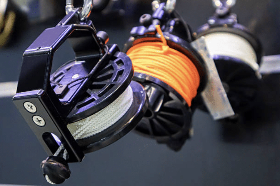 Screenshot 2026-03-16 at 012527 - N9BO℠ | Global Underwater Services Ltd Close-up of three reels with ropes, including one with bright orange cord, mounted on a metal rod. The reels have black plastic frames with screws visible on the side.