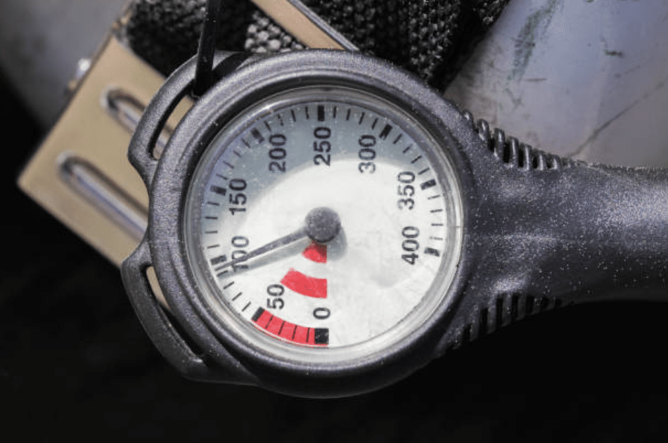 Screenshot 2026-03-16 at 222945 - N9BO℠ | Global Underwater Services Ltd Close-up of a scuba diving pressure gauge, showing the needle pointing just below 50 bar, indicating low air pressure. The gauge is attached to diving equipment, with part of a cylinder visible in the background.
