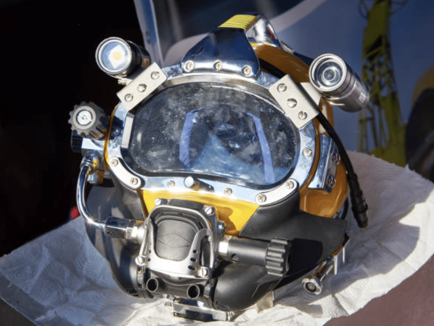 Screenshot 2026-03-16 at 224102 - N9BO℠ | Global Underwater Services Ltd A close-up of a yellow and black commercial diver’s helmet with attached lights and breathing apparatus, resting on a white cloth.
