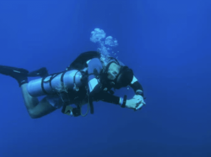 Screenshot 2026-03-16 at 232911 - N9BO℠ | Global Underwater Services Ltd A scuba diver in full kit is underwater, surrounded by deep blue water, with bubbles rising above their head as they swim horizontally.