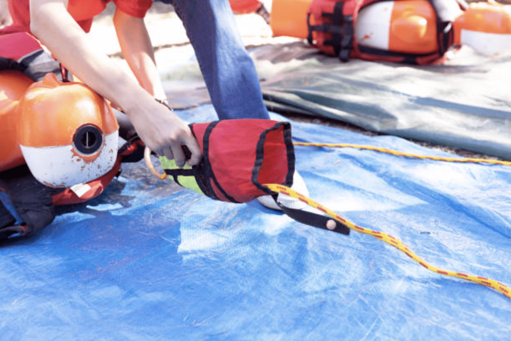 Screenshot 2026-04-01 at 105719 - N9BO℠ | Global Underwater Services Ltd A person packs a coiled rope into a red throw bag on a blue tarpaulin, with life jackets and other rescue equipment visible in the background.