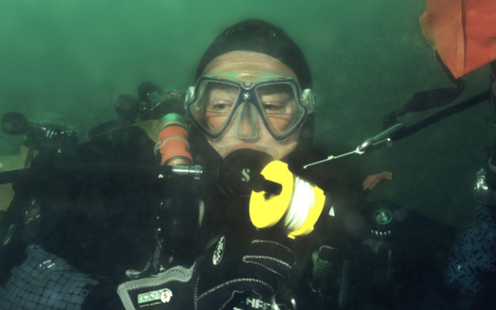Screenshot 2026-04-05 at 180511 - N9BO℠ | Global Underwater Services Ltd A scuba diver underwater wearing a mask, gloves, and wetsuit holds a yellow reel with scuba gear visible in the background.