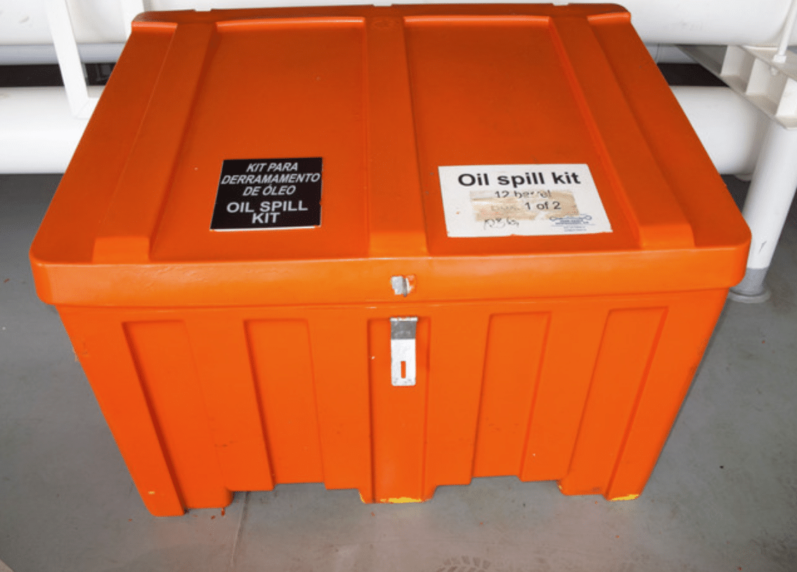 An orange plastic container labelled OIL SPILL KIT and Kit para derramamento de óleo sits on a grey floor, secured with a metal latch.