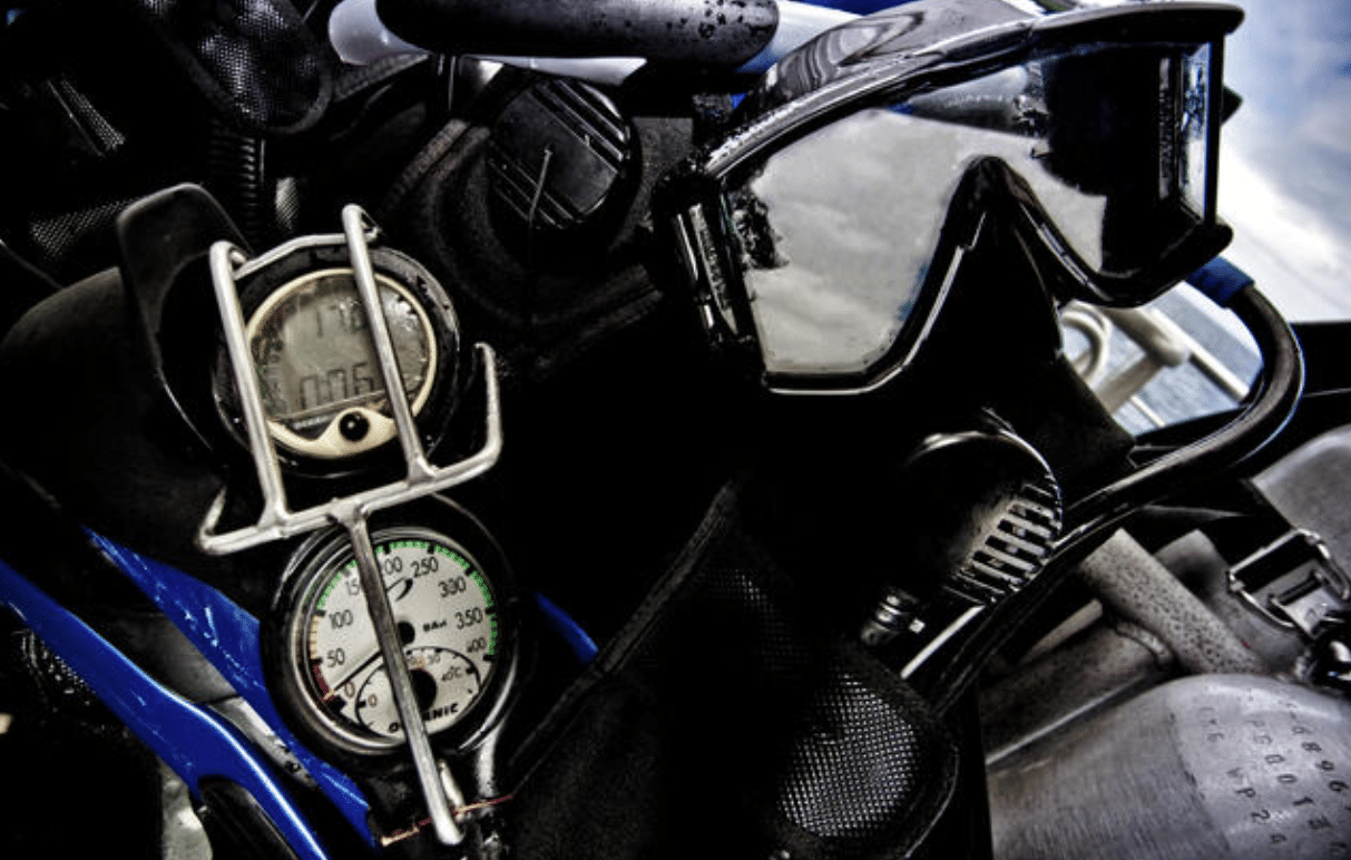 Screenshot 2026-04-06 141446 - N9BO℠ | Global Underwater Services Ltd Close-up of scuba diving equipment, including a mask, pressure gauges, regulator, and parts of a dive cylinder, with reflections visible on the mask’s lens.