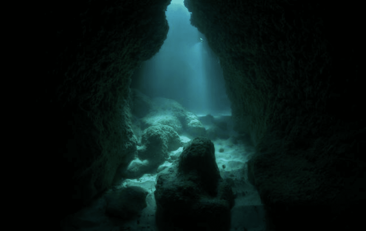Screenshot 2026-04-06 154001 - N9BO℠ | Global Underwater Services Ltd Sunlight filters through the water, illuminating an underwater cave with rocky walls and a sandy floor, creating a mysterious and serene atmosphere.