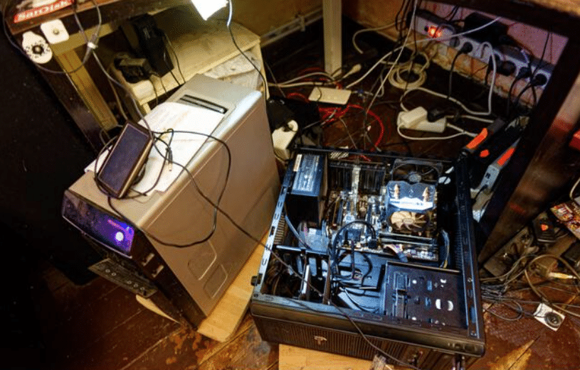 Screenshot 2026-04-07 100825 - N9BO℠ | Global Underwater Services Ltd An open desktop computer case with visible internal components sits on the floor next to an older computer tower, surrounded by tangled cables and power strips under a desk.