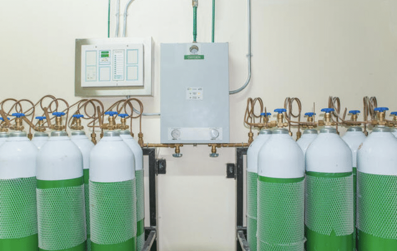 Screenshot 2026-04-07 170328 - N9BO℠ | Global Underwater Services Ltd Rows of green and white oxygen cylinders are connected by copper pipes to a central control unit mounted on a wall in a medical or industrial setting.