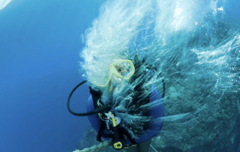 Screenshot 2026-04-07 182749 - N9BO℠ | Global Underwater Services Ltd A scuba diver underwater with yellow goggles and scuba gear is being hit by a splash of water, creating bubbles and turbulence around their head near a rocky area.