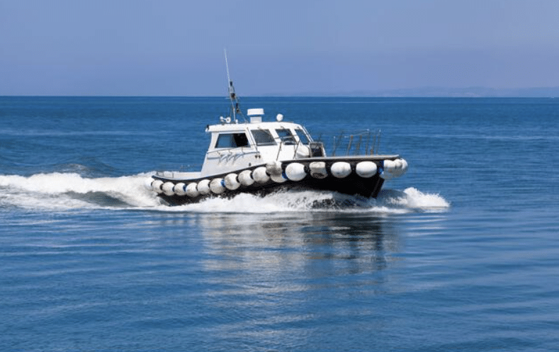 Screenshot 2026-04-07 210609 - N9BO℠ | Global Underwater Services Ltd A small motorboat with fenders along its sides moves quickly across calm, blue water, leaving a trail of white waves behind it under a clear sky.