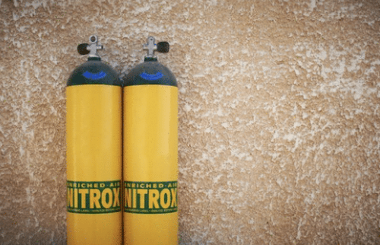 Screenshot 2026-04-15 at 203740 - N9BO℠ | Global Underwater Services Ltd Two yellow scuba diving cylinders labelled ENRICHED AIR NITROX stand upright side by side against a textured beige wall.