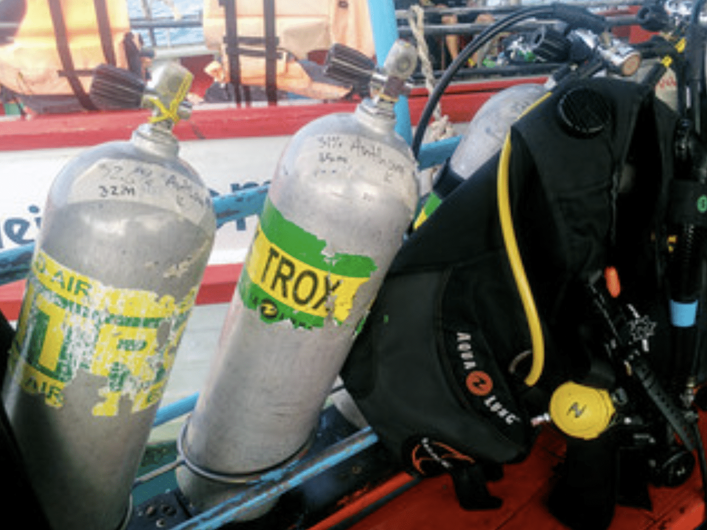 Screenshot 2026-04-15 at 203943 - N9BO℠ | Global Underwater Services Ltd Three scuba diving cylinders, including one labelled “NITROX,” are secured on a boat next to a black diving vest and regulator, with water and life jackets visible in the background.