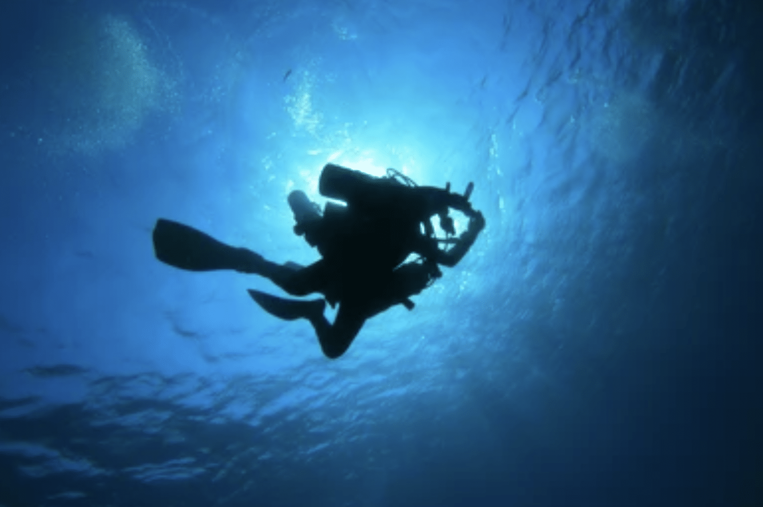 Screenshot 2026-04-15 at 221544 - N9BO℠ | Global Underwater Services Ltd Silhouette of a scuba diver underwater, surrounded by blue light with the sun shining above and bubbles rising towards the surface.