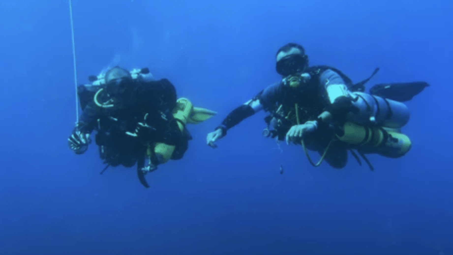 Screenshot 2026-04-16 at 180256 - N9BO℠ | Global Underwater Services Ltd Two scuba divers in full kit are underwater in clear blue water, each holding onto equipment and surrounded by bubbles, floating side by side.