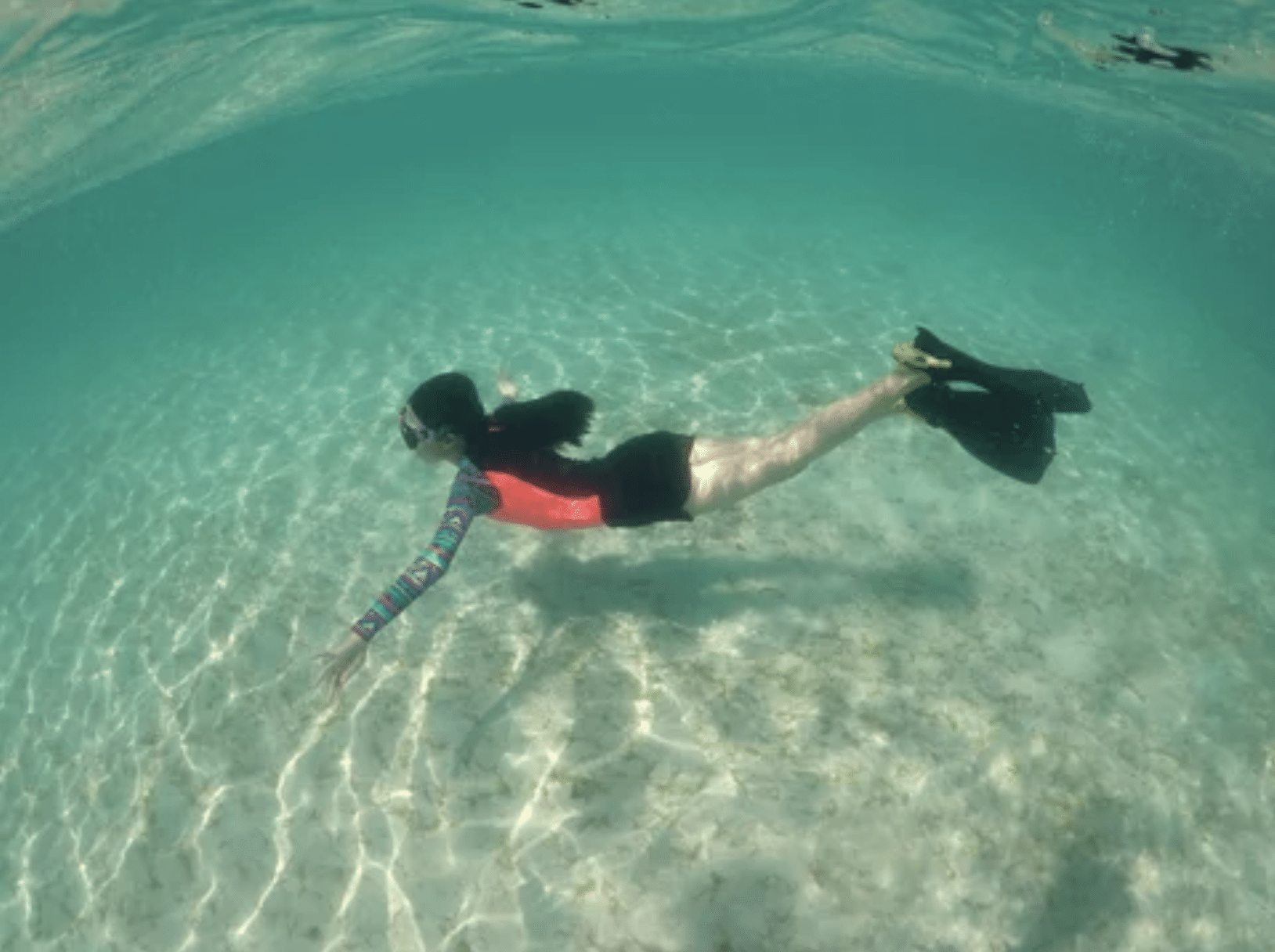 Screenshot 2026-05-18 at 003517 - N9BO℠ | Global Underwater Services Ltd A person wearing a snorkel and fins swims underwater over a sandy seabed in clear, turquoise water. Sunlight creates patterns on the sand, and the swimmer is reaching forward with both arms.