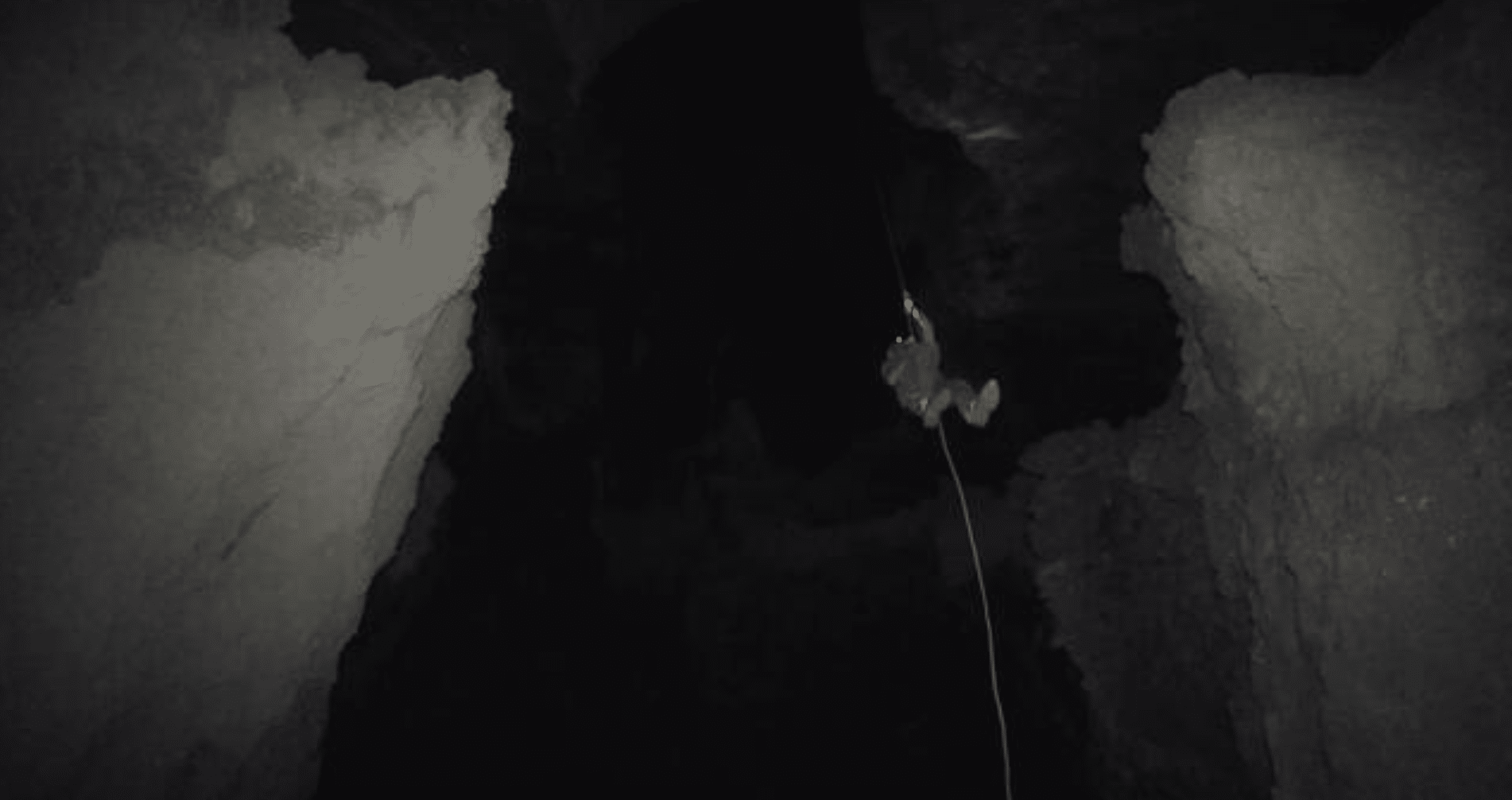 Screenshot 2026-05-23 at 232041 - N9BO℠ | Global Underwater Services Ltd A person wearing a headtorch is suspended by a rope, abseiling down into a dark, rocky cave with large jagged walls on both sides.
