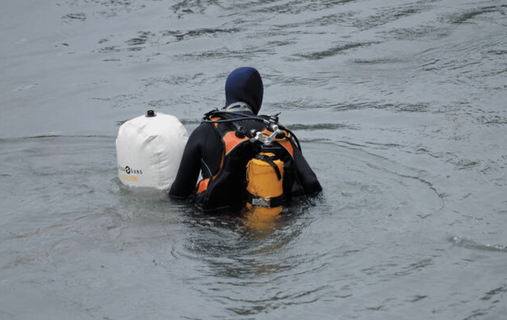 Screenshot 2026-05-27 at 225943 - N9BO℠ | Global Underwater Services Ltd A person in a wetsuit and scuba gear holds a large white floating device while wading in calm water.