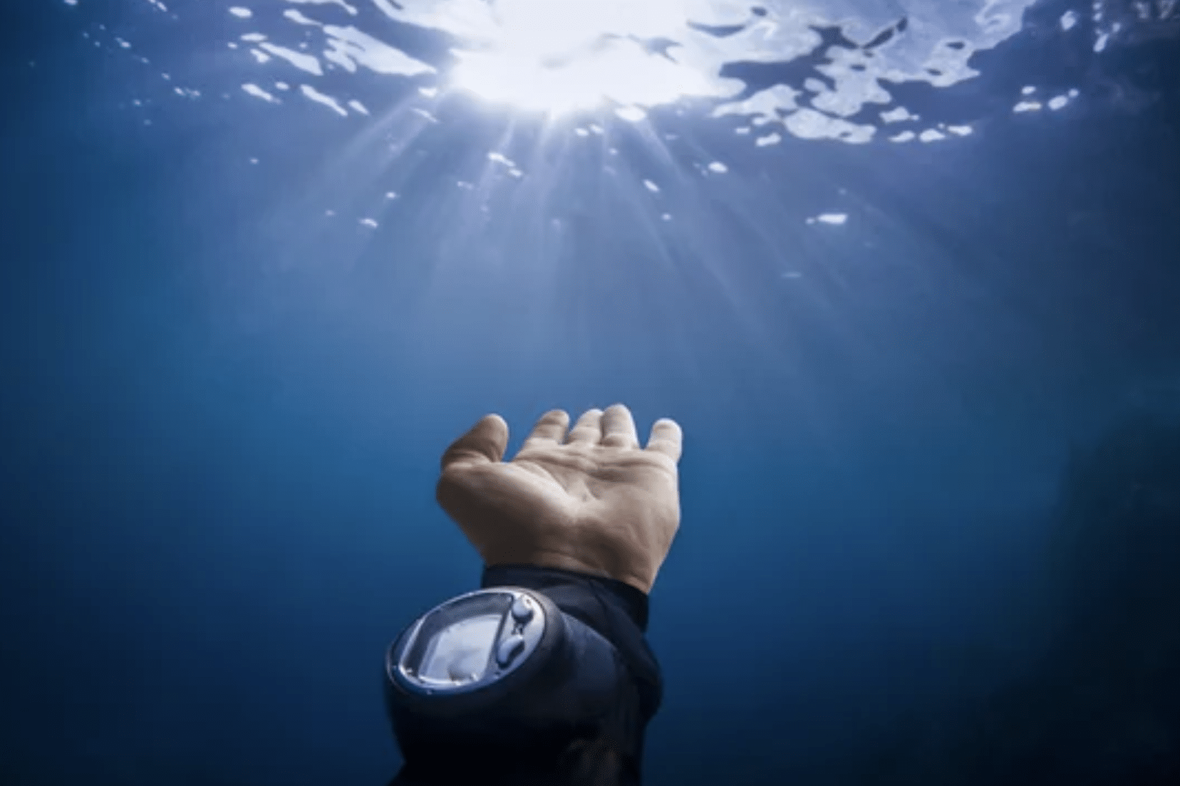 Screenshot 2026-05-28 at 220844 - N9BO℠ | Global Underwater Services Ltd A diver’s hand, wearing a diving watch, reaches up towards the sunlit water surface from underwater, with rays of sunlight streaming through the blue water.
