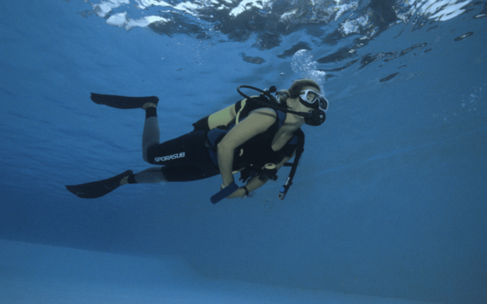 Screenshot 2026-06-02 at 065847 - N9BO℠ | Global Underwater Services Ltd A person wearing scuba gear and fins swims underwater in a clear blue pool, looking ahead and holding a small object.